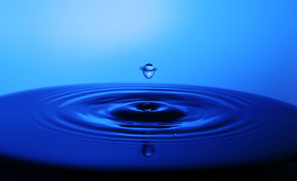 A striking close-up of a water droplet creating ripples on a blue surface, captured in motion.