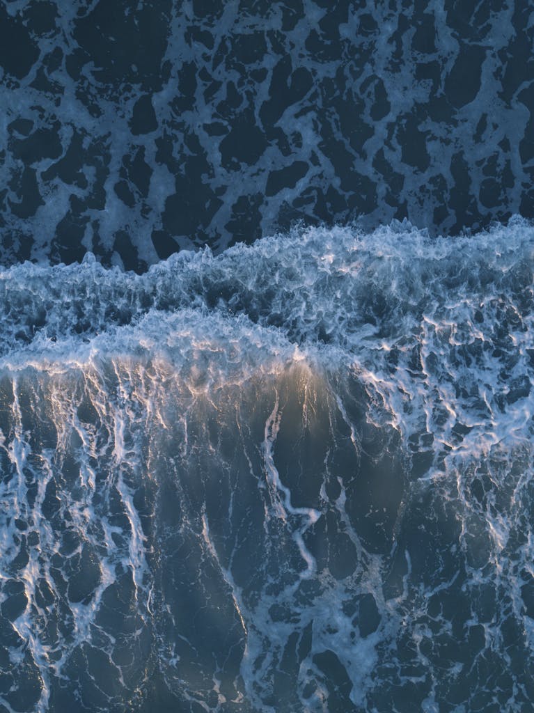 Breathtaking aerial view of crashing ocean waves at sunset, showcasing nature's beauty.